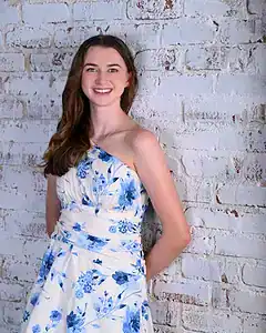 Young woman smiling with a floral dress against a white brick wall.